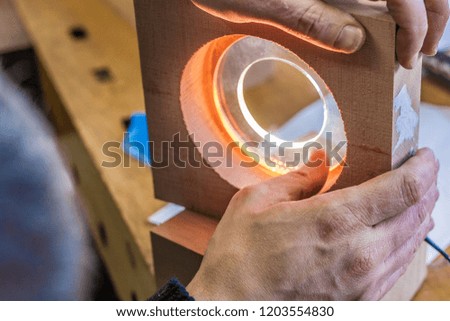 Futuristic round wood and glass lamp. Eco-friendly woodworker's shop. Details and focus on the texture of the material, sawdust, lighting and transparent elements. Organic design. 