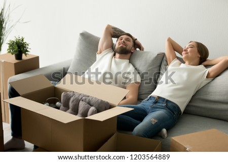 Calm relaxing couple sitting together on couch at new house after moving, family just arrived in new home, man and woman start living together, laying together on sofa, feeling tired after unpacking Royalty-Free Stock Photo #1203564889