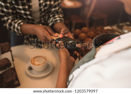Closeup of a young African woman paying for her purchase with a credit card machine while standing at a counter in a cafe