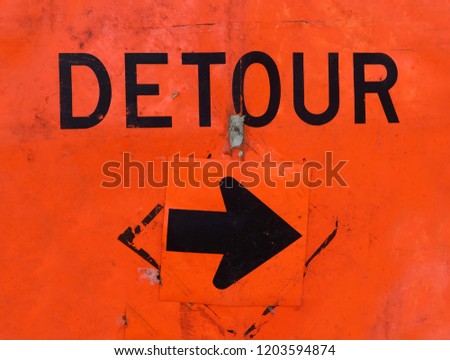 Battered orange DETOUR sign with arrow.