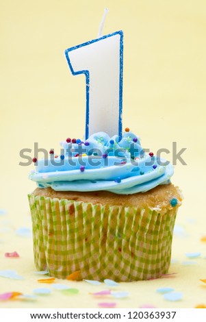 Close-up shot of a cupcake with number 1 birthday candle over yellow background.