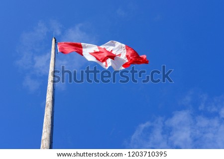 Canadian flag in blue sky background, fluttering in wind, sunny day