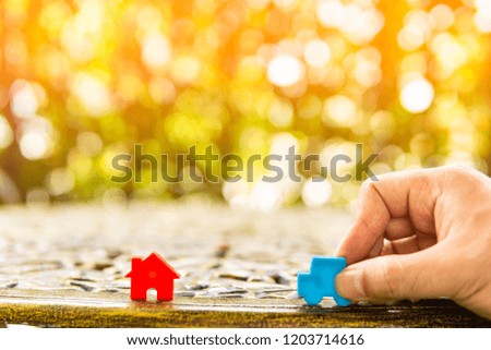 Hand hold blue car model and red home model on table.Have a solar background. Home loan with car exchange or trade in business or real estate.For family happiness.