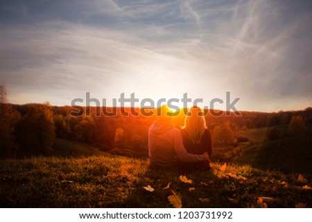 
Very beautiful young couple in love guy with a girl sitting on the edge of a hill and watch the sunset outdoors