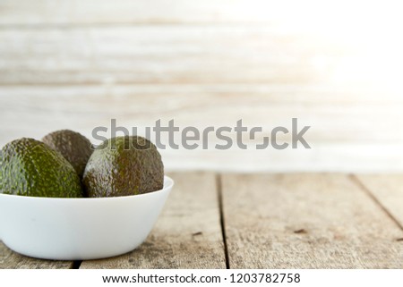Avocado on old wooden table.Halfs on white bowl. Fruits healthy food concept. empty space. Natural morning sunshine on the left side.