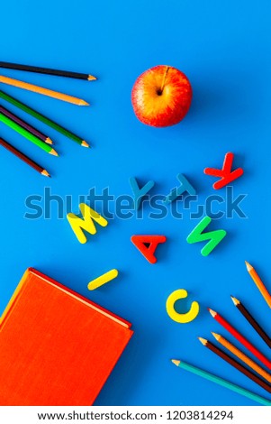 Primary school concept. Letters of english alphabet, book, apple and color pencils on blue background top view