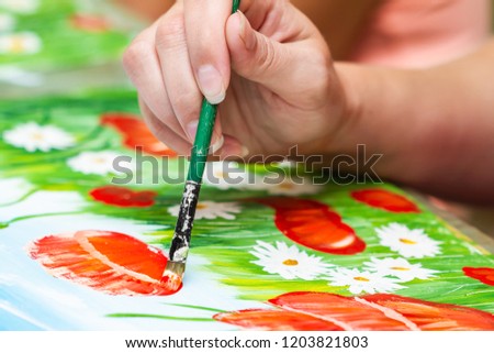 A girl paints a picture by gouache. A girl drawing poppies and chamomiles. The hand and paint brush. Closeup, selective focus