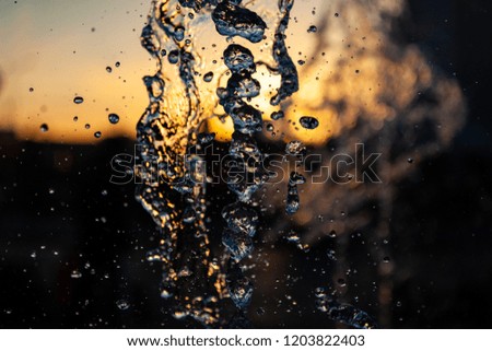 Jets of water with a lot of drops and bubbles under the sun on a yellow-orange background. A large plan The texture of the water waves of a large fountain