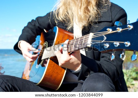 Closeup of a young female (no face pictured) playing an acoustic guitar, wearing mostly black. 