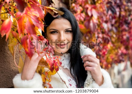 Woman in fashion dress posing with yellow leaves in park