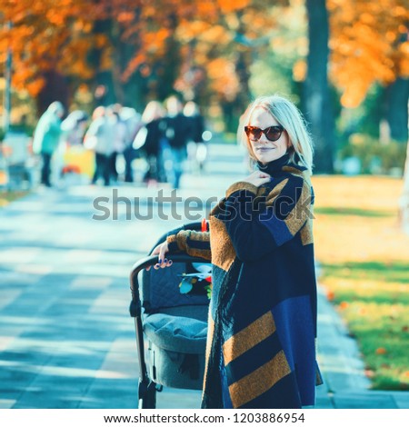 A young mother with a stroller walks through the autumn park. Walking with an infant in the open air in a pine forest. Newborn, family, child, parenthood.