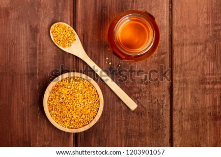 Healthy organic food. Bee pollen, a jar of honey, and a wooden spoon, shot from the top on a dark wooden background with copy space