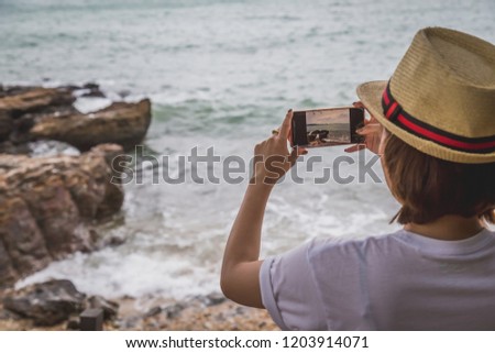 Lonely Asian woman traveler standing and photographing near the sea