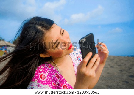 young happy and beautiful Asian Chinese woman taking selfie picture with mobile phone camera at tropical paradise beach during summer holidays travel smiling cheerful and sweet