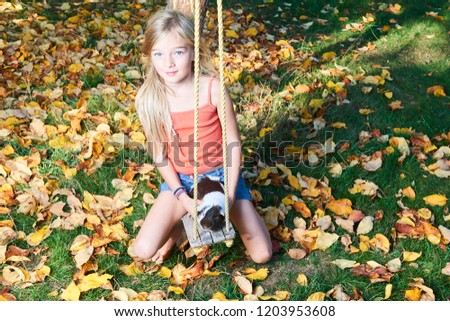 Cute child girl sitting on swing in garden and playing with guinea pig pet animal