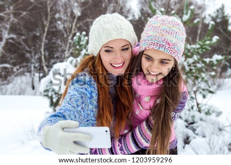 Mom and daughter are photographed in a winter forest, family values. Two girls make a photo. Selfie on phone in winter. Family of mother and her  daughter outdoors on beautiful winter day with snow. 