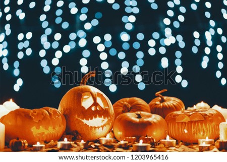 Table with autumn leaves, candles and carved pumpkins in real photo with lights in blurred background