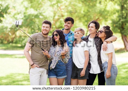 friendship, leisure and technology concept - group of happy smiling friends taking picture by selfie stick at summer park