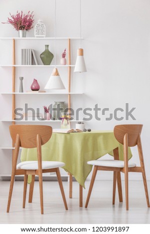 Vertical view of wooden chairs at round table with olive green tablecloth in bright elegant living room, real photo
