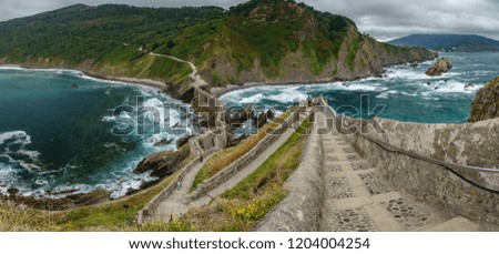 Ultra wide panorama top view of stairs to San juan de Gaztelugatxe chapel with blurred tourists. Basque Country