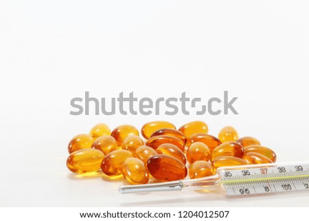 Cod liver oil capsules and mercury thermometer on white background.