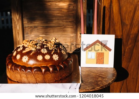 Close-up house made of wooden tangram puzzle over desk with wedding bread korovai near it on the wooden background