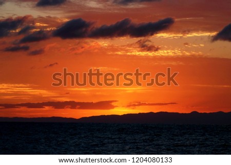 Amazing blazing sunset landscape at black mount, dark waving sea, and yellow-orange sky above it with sun golden reflection as a background. Beautiful summer sunset viewing on the beach.