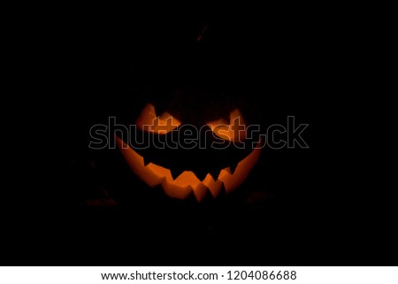 Halloween pumpkin smile and scrary eyes for party night. Close up view of scary Halloween pumpkin with eyes glowing inside at black background. Selective focus