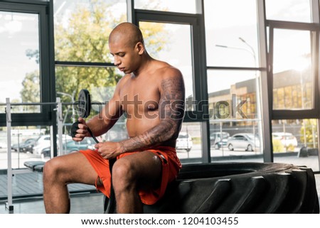 shirtless african american sportsman wrapping hand in boxing bandage at gym