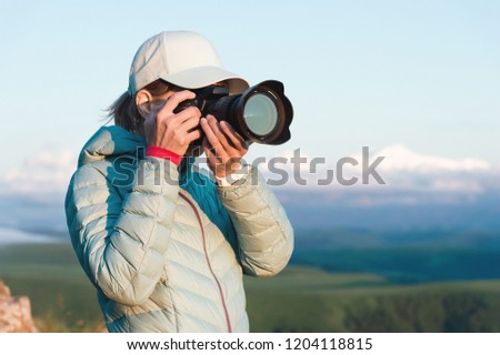 Portrait of a girl photographer in a cap on nature photographing on her digital mirror camera. Front view