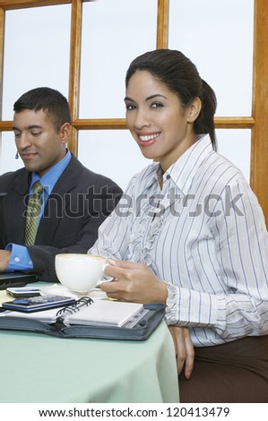 Portrait of a happy business woman holding cup of coffee with colleague in the background