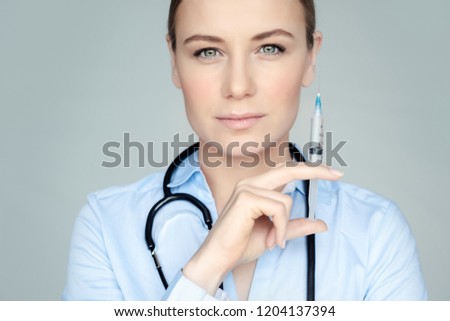 Portrait of a serious woman doctor with syringe in hand isolated on gray background, injections, plastic surgery and beauty treatments concept