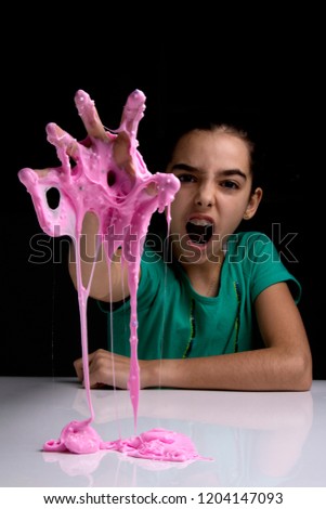 Cute girl playing with a sticky pink slime toy. Studio isolated on black background.
