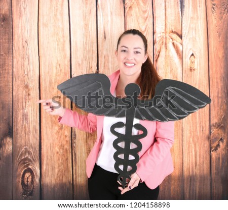 Young business woman holding a medical sign while pointing her finger to one side against a wooden background