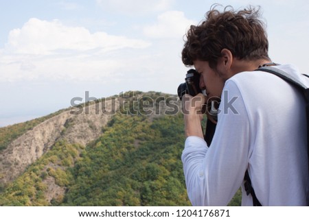 Young curly traveler taking photo with camera in mountains near sighnaghi, Georgia.