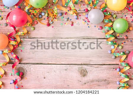 Carnival background with balloons and streamers forming a border around rustic pink tinged wood with copy space