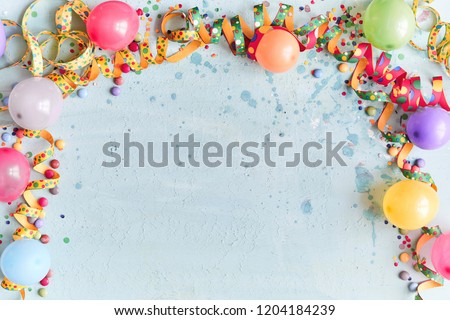 Carnival, festival or birthday balloon background with colorful party streamers, candy and confetti making a border on a blue background with copy space