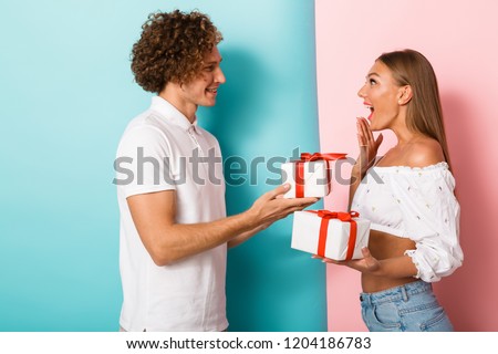 Excited young couple standing isolated over double colored background, exchanging with gift boxes