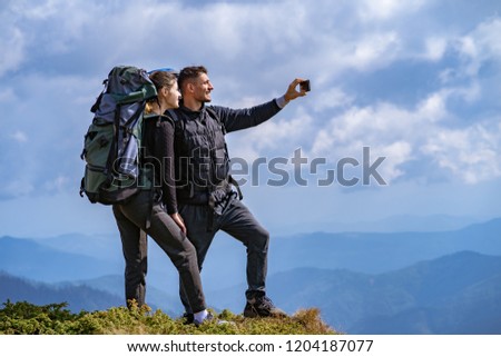 The happy couple with backpacks take a selfie on the cliff