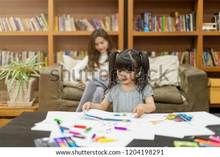 beautiful attractive caucasian child  girl doing painting with  mother read book behind house family ideas concept
