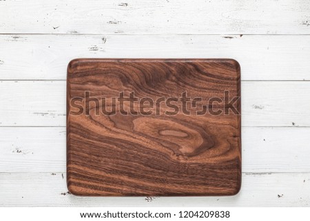 Handmade pecan rectangular rounded wooden chopping board on a white wooden board top. Walnut texture background. Kitchen workbench background.