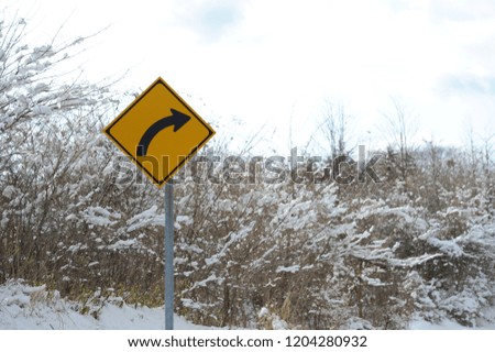 Traffic sign turn right on snowy road. Close-up. Background with cloudy sky and dry branches of trees with snow. Shizuoka Prefecture, Japan. Winter of February 2011.