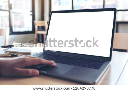 Mockup image of a hand using and touching laptop touchpad with blank white desktop screen while sitting in office