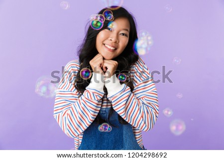 Image of happy young asian beautiful attractive woman posing isolated indoors over soap bubbles.