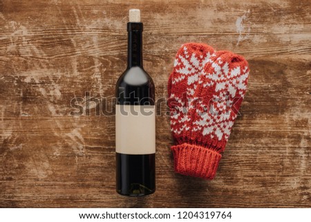 top view of wine bottle and winter mittens on wooden tabletop, christmas concept