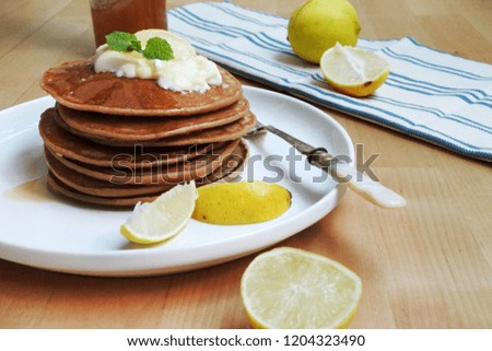 Fluffy lemon greek yogurt pancakes drizzle with honey, topped with lemon slice and mint leaves on white plate with a vintage silver fork, lemon on cloth placemat on wooden table