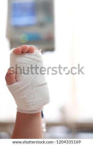 Soft focus at bandage cover on baby hand and Saline intravenous on hand. Background with blurry medical treatment machine. Copy space and Concept of kid recovery, medical treatment, get well soon.