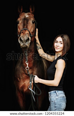 Portrait of smiling pretty woman standing by horse on the black background. Isolate