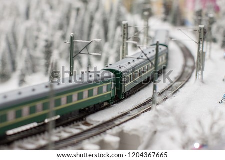 model with a picture of a miniature in Russia on a winter day when a train with passenger cars crosses the snow-covered expanses on the background of the forest sprinkled with snow and power poles