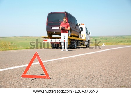 Emergency stop sign and man near tow truck with broken car on background